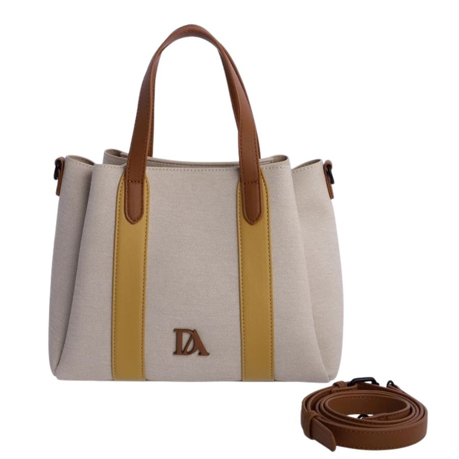 Bolso Tote Mujer Chic. Vista frontal de bolso tote de lona beige con bandas amarillas, asas marrones y logo metálico DA sobre fondo marfil.